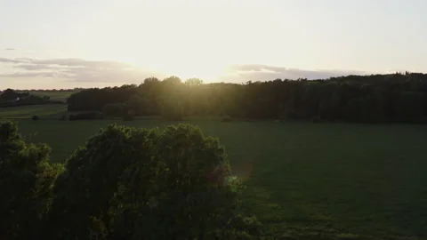 Drone flight against the setting sun over a field and rising in front of a large Stock Footage 163089763