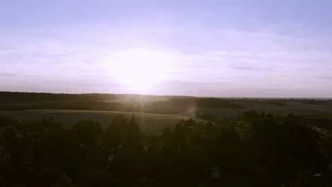 Drone flight against the setting sun over a small town and rising in front of a Stock Footage 163090446