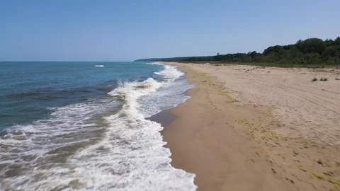 Drone flight along a sandy beach with gentle waves and clear blue sea. Aerial Stock Footage 326047545