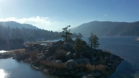 Drone Flight backward over alpine lake revealing wooded island on Big Bear Lake Stock Footage 150200042