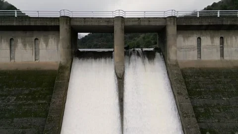 Drone flight backwards over a dam between mountains releasing water Stock Footage 307589932