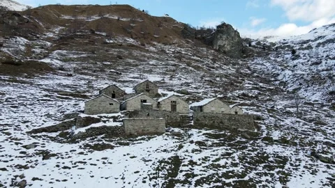 Drone flight in mountain with snow over old constructions (alpine pasture). 4K Stock Footage 148031474