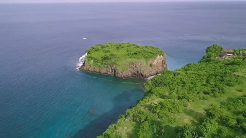 Drone flight over a green cliffside and a green islet at the blue sea. Video stock 137452809