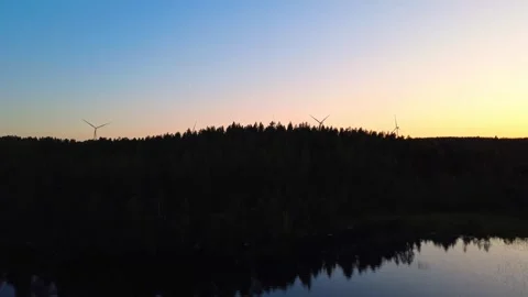 Drone flight over a lake to wind turbines on a wooded hill at sunset, energy Stock Footage 345658818