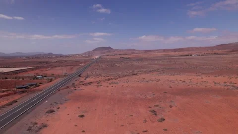 Drone Flight Over Red Desert Road with Distant Mountains in Fuerteventura Stock Footage 309018133