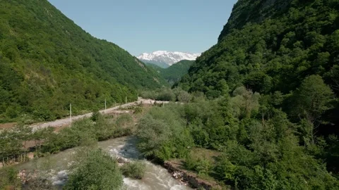 Drone flight over river, green mountains against backdrop snow peak, aerial view Stock Footage 274482573