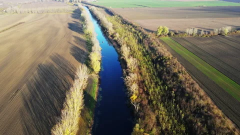 Drone flight over a small river surrounded with agricultural fields and trees Stock Footage 263211649