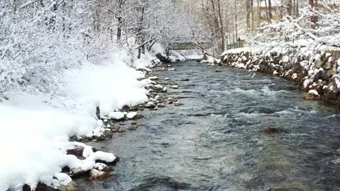 Drone flight over snowy river approaching bridge in winter landscape Stock Footage 327647489