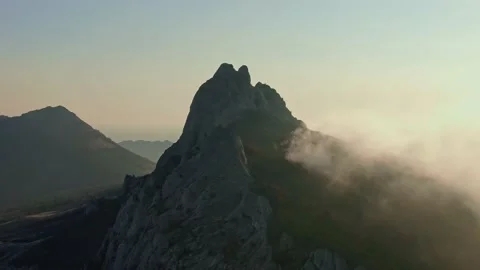 Drone flight over the top of a mountain where trees grow and fog creeps on an Stock Footage 131079211