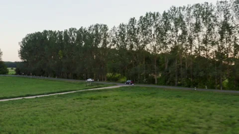 Drone flight parallel to a car on a country road with tall trees and green Stock Footage 163088139