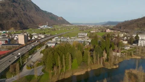 Drone flight parallel to a highway, passing over a calm pond near a small town Stock Footage 321458452