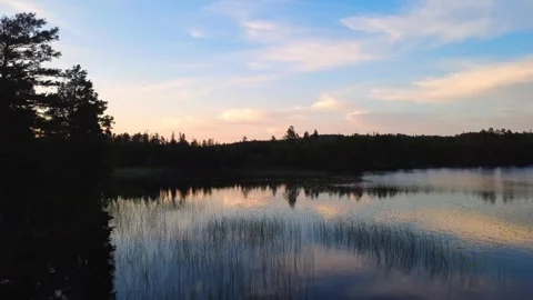 Drone flight at sunset over a lake, with reflections, and forest silhouettes Stock Footage 345658820