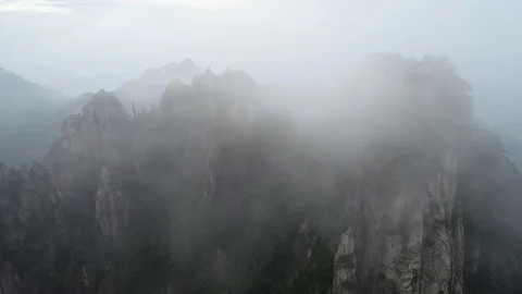 Drone flight through mist fog reveals craggy mountains peaks Huangshan China Stock Footage 99049535