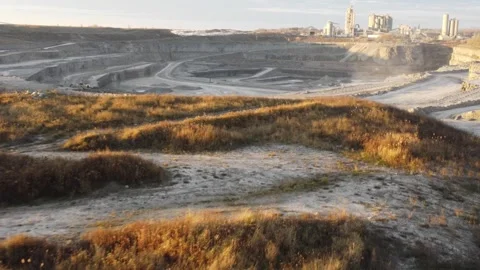 Drone fly across ground into open mine pit with factory in background 스톡 동영상 251257059