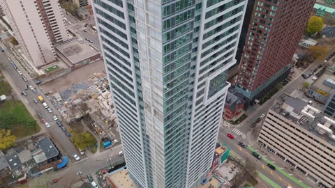 Drone flyby beside a modern condo tower with road traffic and autumn park below Stock Footage 330036746
