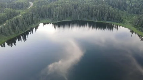 Drone flying above a small round northern lake reflecting a clear blue sky, Stock Footage 329867970
