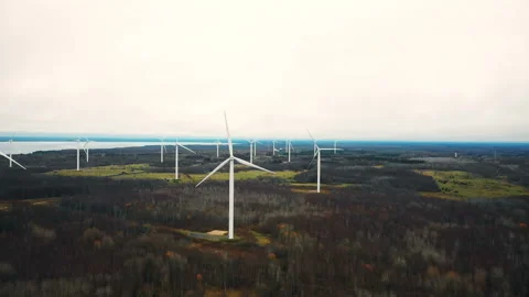 Drone flying above, tilts down on windmill turbine farm working at autumn forest Vidéo 149422071