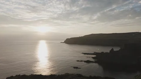 Drone flying across field into sunset over coastline across the ocean Stock Footage 277623112