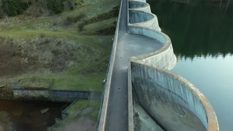 Drone flying along dam toward woman walking, cinematic aerial perspective Video stock 333060975