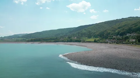 Drone Flying Back Over Waves Hitting Beach at Coastal Town Porlock Weir Stock Footage 336195246