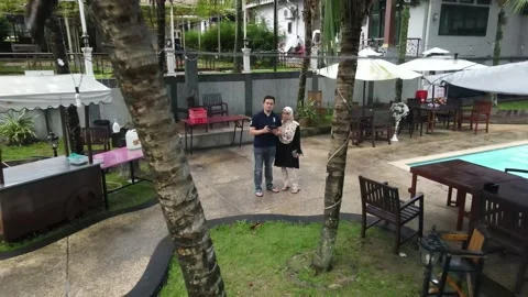 Drone flying backward from couple and passing through tree and garden Stock Footage 149947513