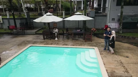 Drone flying backward from swimming pool and couple Stock Footage 149869739