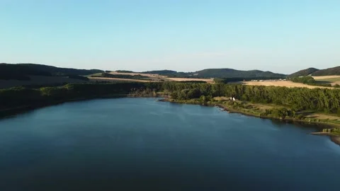Drone flying backwards over the peaceful and idylic blue lake on sunset Stock Footage 201967521