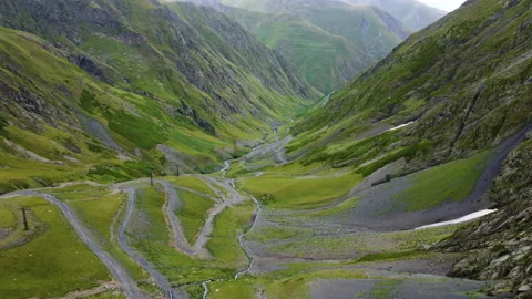 Drone flying between mountains above green rocky valley with serpentine road Stock Footage 229858341