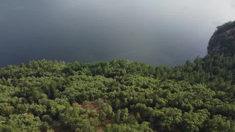 Drone flying down hill over forest hill towards large lake with deep blue water Stock Footage 280012759