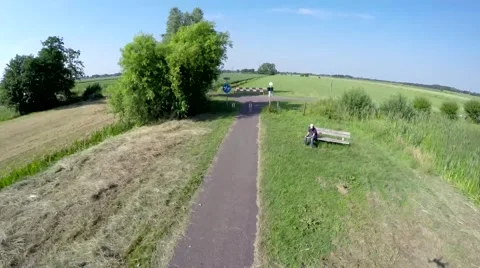 Drone flying fast and low over a concrete cycling path passing bench and trees Stock Footage 52119708