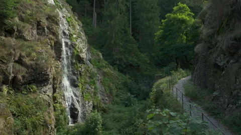 Drone flying forward over a historic trail next to a beautiful cascade in a lush Stock-Footage 333050677