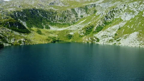 Drone flying forward over lake surrounded by rocky green mountains Stock Footage 314199360