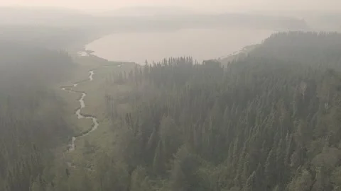 Drone flying low over a boreal forest and small lake surrounded by trees smoke Stock Footage 158168185