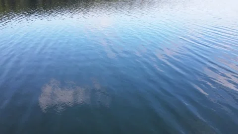 Drone flying low over a calm lake that is reflecting a blue sky with white Stock Footage 330363964