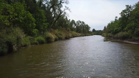 Drone flying low over water surface of canal amidst countryside greenery. Stock Footage 220848994