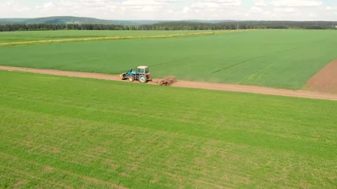 Drone flying over field and blue cultivation tractor driving on a ground road. Stock Footage 143372104