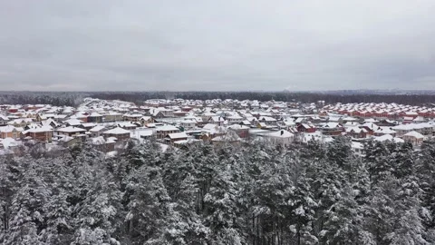 Drone flying over forest towards cottage village covered by snow Видео 188037966