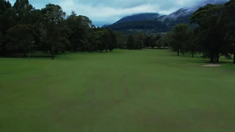 Drone flying over a green forest and golf course, mountain and cloudy sky 動画素材 248757323