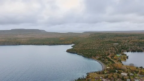 Drone flying over the lake surrounded by dense forest and cottages Stock Footage 126078901