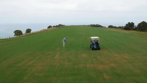 Drone flying over man swinging at golf on cliffside golf course Stock Footage 86707499