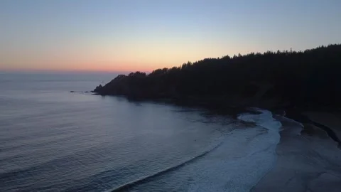 Drone Flying Over Ocean Waves Past Pine-Covered Coastal Cliffs at Sunset Stock Footage 341366600