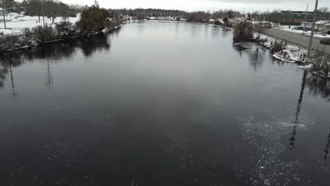 Drone flying over river in winter with cars drving by and snow on trees 스톡 동영상 296489998