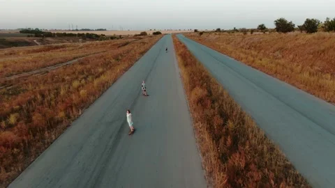 Drone is flying over a road where three women are longboarding, 4k Stock Footage 142368353