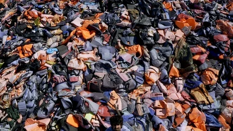 Drone flying over Sad Man sitting in Huge piles of lifejackets and clothes Stock Footage 126318120
