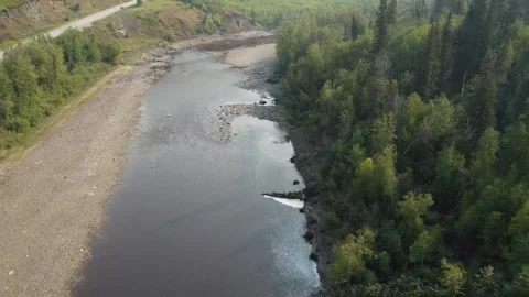 Drone flying over shallow river with rocky shoreline with large hills and trees 스톡 동영상 252777900