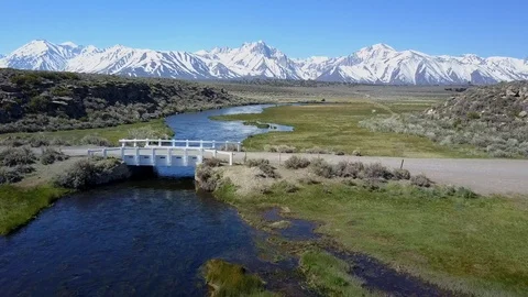 A drone is flying over a small river, there is a tiny brigde crossing the Stock Footage 100562735