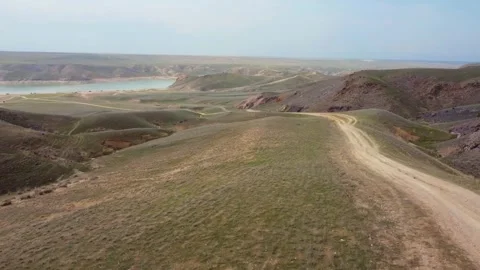 Drone flying over spring steppe with dirt road, hills and Reservoir in KZ Stock Footage 332985033
