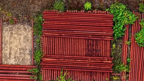 Drone flying over stacked red metal pipes at a construction site Stock Footage 346582997
