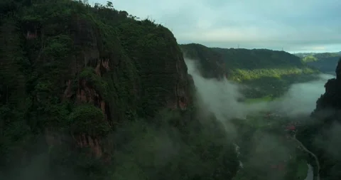 Drone flying over steep cliff with fog drifting across mountain valley Video stock 333407755