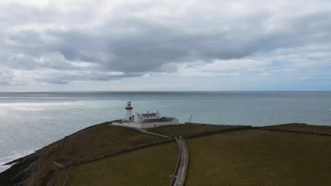 Drone flying over a white lighthouse on a green rock near the ocean, Ireland Stock Footage 267076629